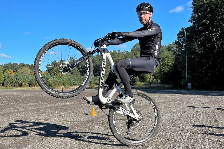 Emil Lindgren med cykelkläder, svart Lazer hjälm, vit MTB-cykel med Shimano XTR och PRO-komponenter som cyklar på bakhjulet.