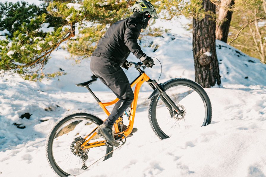 Vinterkledd terrengsyklist som sykler opp en bakke med snø.