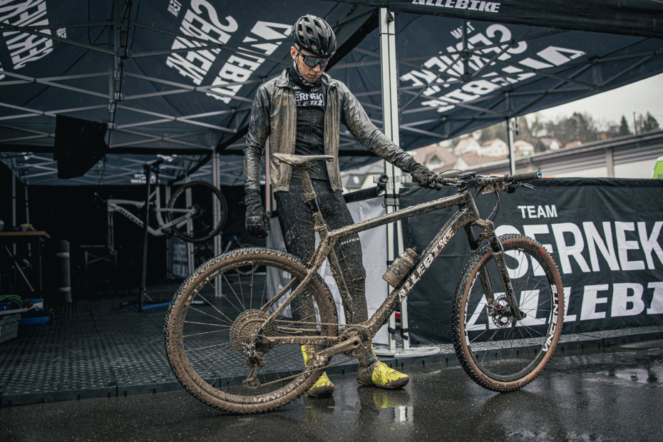 MTB-cyklisten Oscar Lind står och tittar ner på sin mountainbike – båda han och cykeln är täckta i lera.
